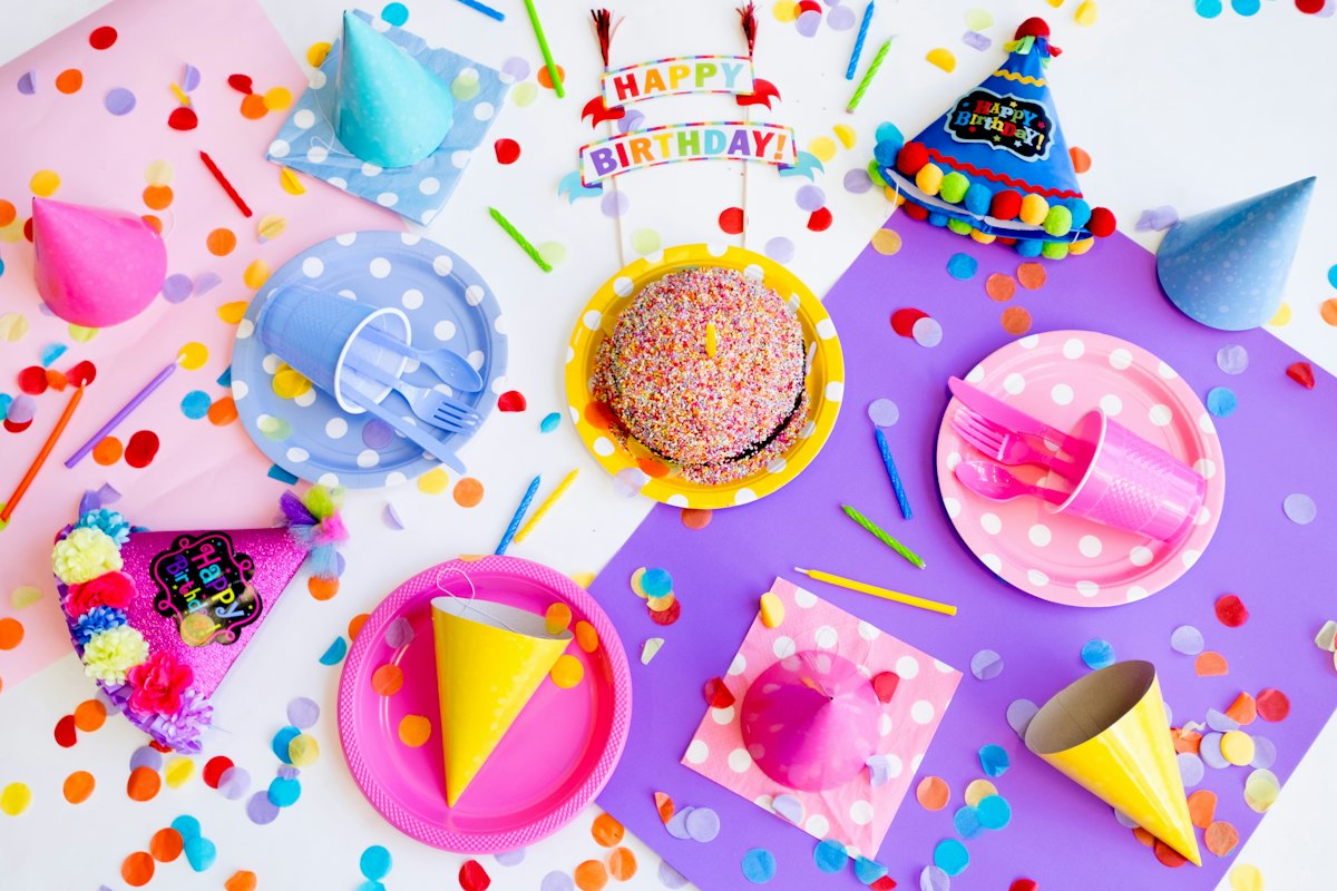 A colourful birthday party table with plates, cups and party hats